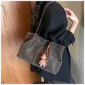 Detail of dark brown faux suede tote bag with contrast white stitching and bear charm