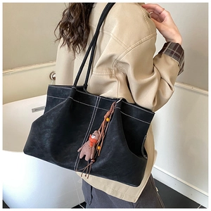 Detail view of large black suede tote bag with white stitching and bear charm