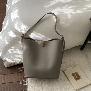 Détail du sac seau en cuir gris avec fermoir rotatif doré et logo de marque embossé