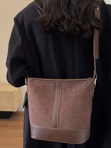 Vintage brown suede bucket bag worn crossbody over a black coat for autumn winter fashion
