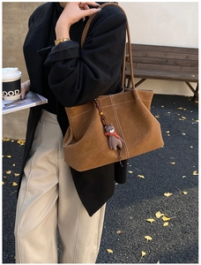 Close-up of brown suede tote bag with white stitching and a cute bear charm accessory
