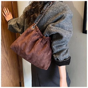 Detail of a brown suede bucket bag with pleated drawstring and metal chain strap