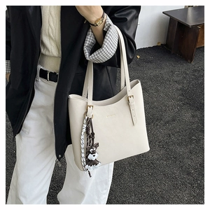 Detail of minimalist cream tote bag with fine leather texture and cute dog charm hanging
