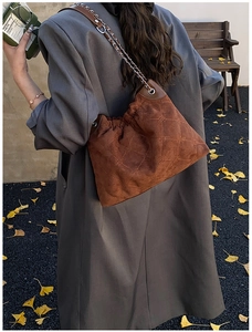Close-up of brown quilted suede bucket bag with silver metal chain on autumn street