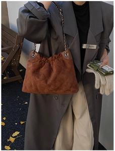 Detail of dark brown suede bucket bag with quilted patterns and chain strap in street setting