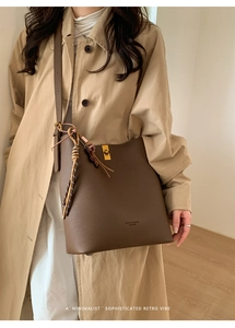 Détail du sac à bandoulière en cuir marron foncé avec fermoir doré et pompon tissé