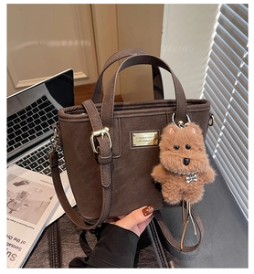 Detail of a brown leather tote bag featuring a plush dog charm and gold fashion logo plate