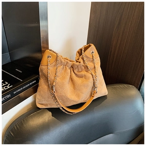 Detail of tan suede quilted bucket bag with chain strap next to interior design books