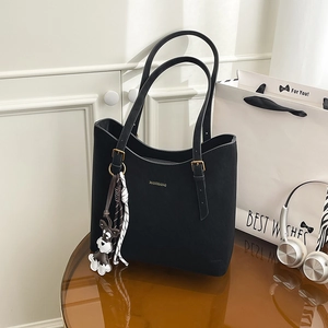 Detail of black leather tote bag featuring gold MANXIANG logo and cute dog charm pendant