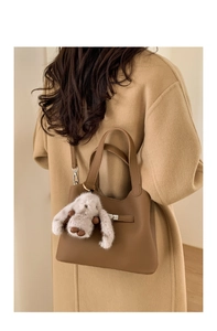 Detail of dark brown leather bucket bag with plush rabbit charm and silver metal clasp