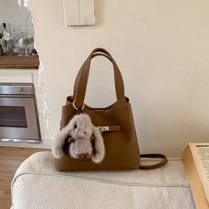 Detailed view of brown lychee grain bucket bag with silver lock and plush bunny pendant