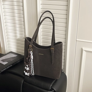 Detail of a dark brown suede tote bag with a golden logo and a cute dog charm on a sofa
