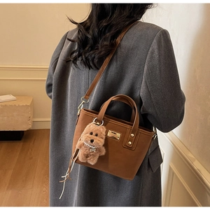 Close-up of brown matte leather handbag with gold accents and cute plush dog charm