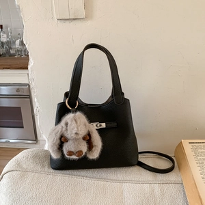 Detail of black lychee grain leather bucket bag with silver metal lock and plush rabbit charm