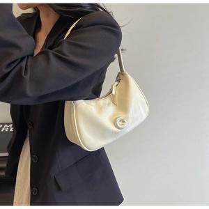 Détail d'un sac hobo beige avec boucle en C argentée porté sur un blazer noir élégant