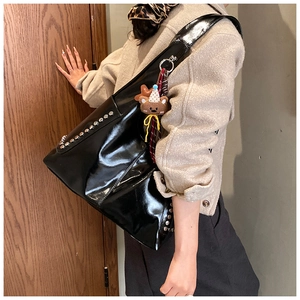 Details einer schwarzen Lackleder-Hobo-Tasche mit silbernen Nieten und Teddybär-Anhänger