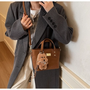 Brown leather handbag styled with a grey suit and a cute plush puppy charm accessory