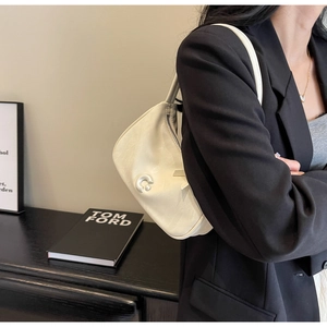 Détail d'un sac à bandoulière en cuir crème avec boucle ronde sur une veste de costume