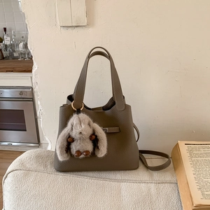 Detail of taupe pebbled leather bucket bag with a cute plush bunny pendant on a sofa