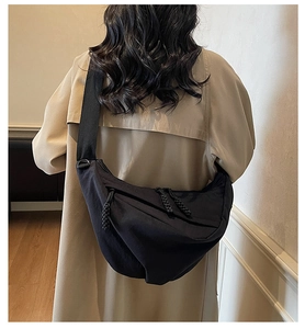 Rear view of model wearing a large black nylon crescent bag with wide strap over a khaki coat