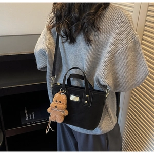 Detail of black leather tote bag with cute brown plush puppy charm and metal logo plate