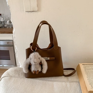 Close-up of dark brown lychee leather bucket bag with silver clasp and grey rabbit charm