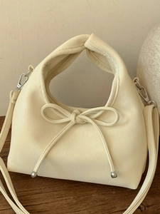Cream pebbled faux leather handbag with ribbon bow detail for women on wood table
