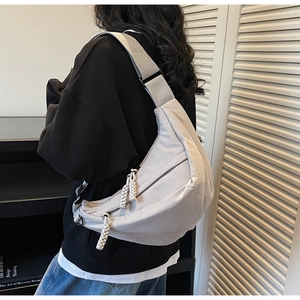 Close-up of a light grey crescent crossbody bag with an adjustable wide strap worn by a person