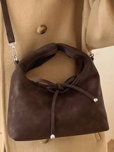 Minimalist dark brown suede handbag with decorative bow strap worn on a camel coat