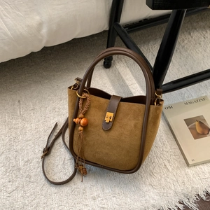 Détail d'un sac seau en daim marron avec garniture en cuir et décoration de gland en bois