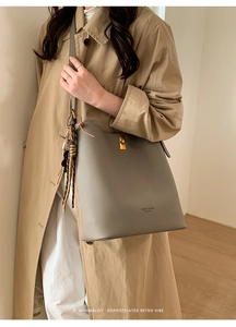 Détail du sac seau en cuir grainé gris avec fermoir doré et pendentif tressé décoratif
