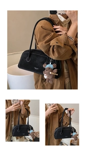 Detail of black suede shoulder bag with contrast stitching and teddy bear pendant
