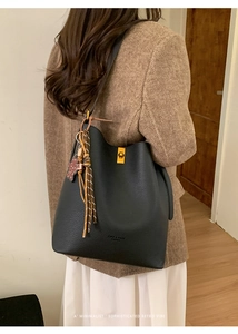 Gros plan sur le sac seau en cuir litchi noir avec boucles dorées et pompon tressé