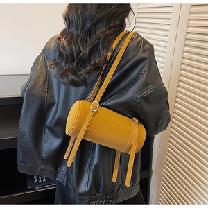 Detail view of bright yellow cylindrical bag with adjustable straps on leather jacket