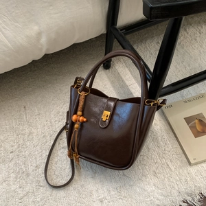 Détail du sac café foncé avec pendentif en bois et boucle dorée sur tapis