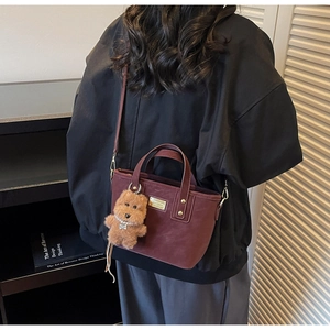 Chic burgundy tote bag with gold hardware and cute puppy charm shown as crossbody style