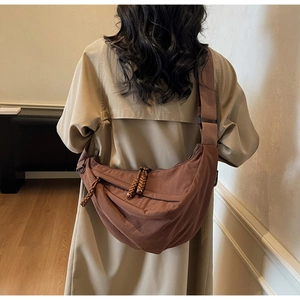 Close-up of brown crescent crossbody bag with woven rope zipper detail on khaki trench coat