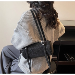 Close-up of black cylinder bag showing matte leather texture and silver buckle detail