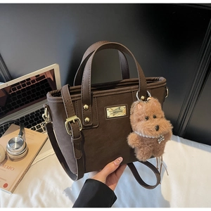 Detail showing dark brown leather tote with plush dog charm and gold metal plate