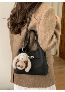 Close-up of black litchi grain bucket bag with silver turn-lock and plush bunny charm