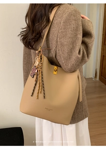 Détail du sac seau en cuir kaki avec fermoir doré et pampille porté par un mannequin