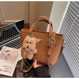 Detail of caramel brown tote bag with plush dog charm and gold metal plaque on office desk