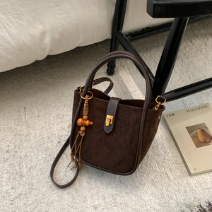 Détail du sac seau marron en daim avec base en cuir et pompon décoratif en perles de bois