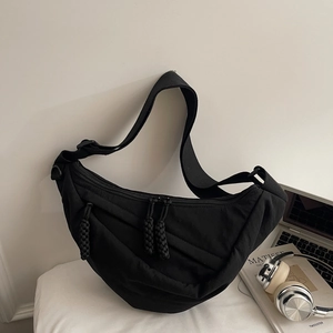 Close-up of black quilted dumpling bag with dual metal zippers and wide nylon shoulder strap