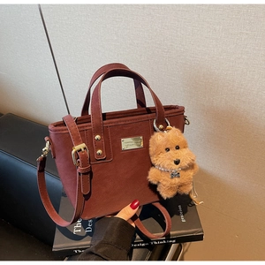 Detail of burgundy PU leather handbag with plush puppy charm and detachable shoulder strap