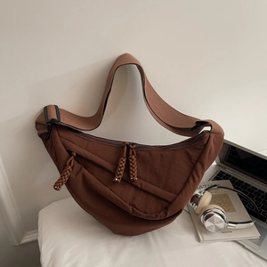 Macro detail of dark brown crescent bag featuring pleated nylon texture and woven zipper