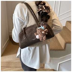 Detail of dark brown faux suede shoulder bag with cute plush bear charm on white stairs