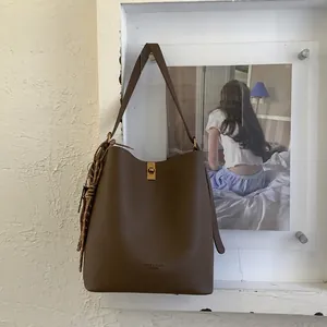 Détail du sac seau en cuir grainé marron avec fermoir tournant doré et pendentif tressé