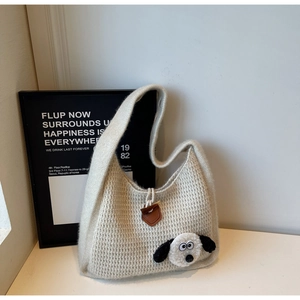 Detail of beige waffle knit tote featuring a plush dog head and brown leather buckle
