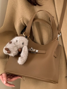 Brown leather bucket bag with silver buckle, plush bunny charm, and crossbody strap